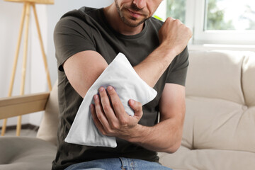 Man using heating pad on sofa at home, closeup © New Africa