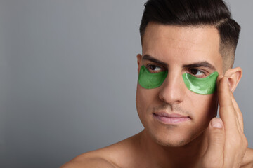 Man applying green under eye patch on grey background. Space for text