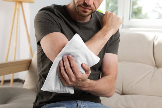 Man using heating pad on sofa at home, closeup