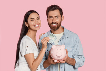 Happy couple with money and ceramic piggy bank on pale pink background