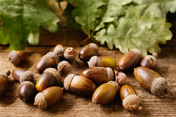 Acorns and green oak leaves on wooden table, closeup