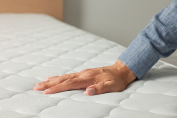 Man touching soft white mattress indoors, closeup
