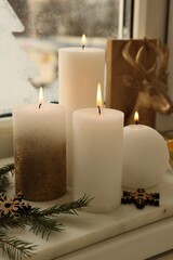 Beautiful burning candles with Christmas decor on windowsill indoors