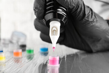 Tattoo artist with professional machine and colorful inks at table, closeup