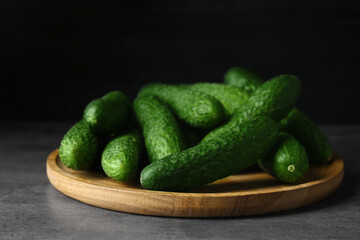 Wooden board with fresh ripe cucumbers on dark grey table