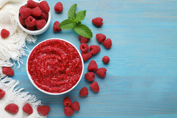 Raspberry puree in bowl and fresh berries on light blue wooden table, flat lay. Space for text