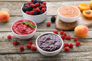 Different puree in bowls and fresh fruits on wooden table