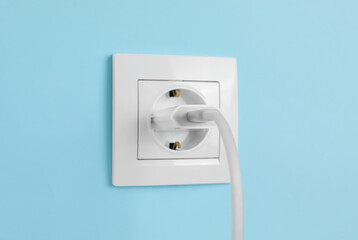 Charger adapter plugged into power socket on light blue wall. Electrical supply