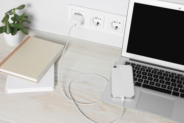 Laptop and smartphone charging on wooden table