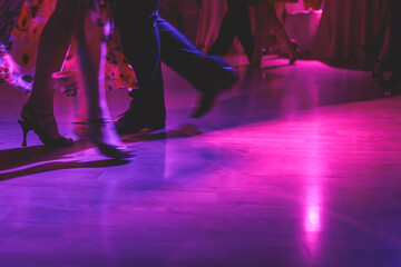 Dancing shoes of a couple, couples dancing traditional latin argentinian dance milonga in the ballroom, tango salsa bachata kizomba lesson, festival on a wooden floor, purple, red and violet lights - obrazy, fototapety, plakaty