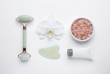 Flat lay composition with gua sha stone and face roller on white background