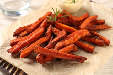Board with delicious sweet potato fries and sauce on table, closeup
