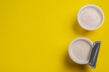 Plastic cups with tasty yogurt on yellow background, flat lay. Space for text