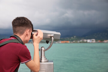 Fototapeta na wymiar Teenage boy looking through mounted binoculars at mountains. Space for text