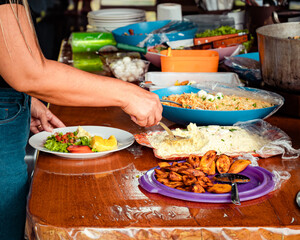 Mulher se servindo comida típica Brasileira, mesa de madeira, com pratos brancos potes azuis, almoço familiar 