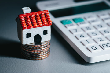 One small model house sitting on top of some coins next to a white calculator White house with red roof real estate investment concept - Powered by Adobe