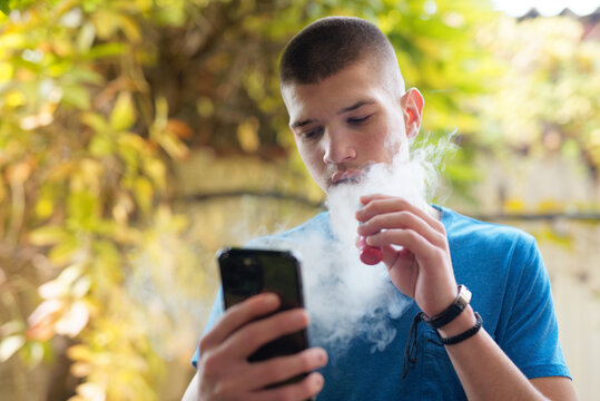 Young man inhaling a smoke of a vape, or electronic cigarette, autumn surrounding