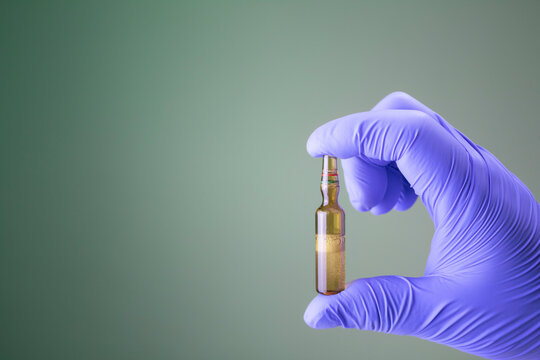 Hand holding an anesthetic container isolated, green background. Lidocaine hydrochloride type bottle. Local analgesic.