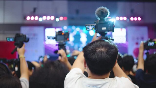 Rear view of man hands taking recording video of live music concert with camera, cameraman filming a concert by a popular music artist, Bright colorful stage light
