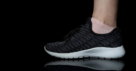 Woman's foot in black sneaker with white sole on dark background with reflection. Space for text.