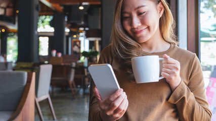 Portrait image of a young woman holding and using mobile phone while drinking coffee in cafe