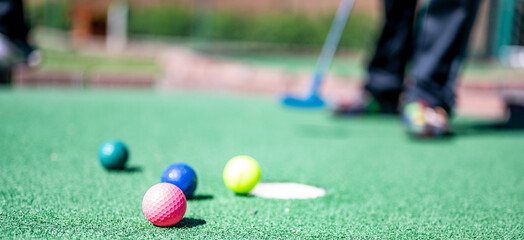 Mini golf game with several colored balls in the way of a putter lined up. - obrazy, fototapety, plakaty
