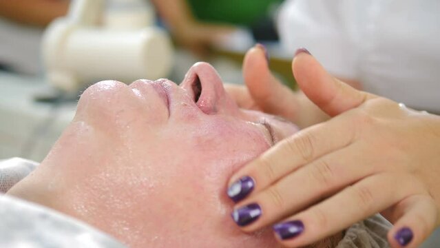 Cosmetologist applying moisturising healing cream after injections on senior woman face skin in modern cosmetology. Beautician ending mesotherapy lifting procedure in beauty clinic. 4 k video