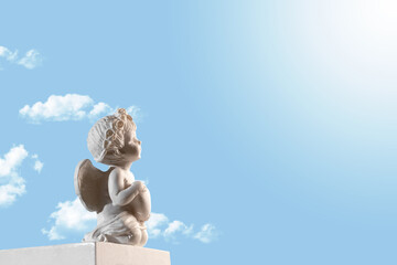 Figurine of an angel Cupid on the podium with a heart on a blu sky with clouds . Valentine's Day.