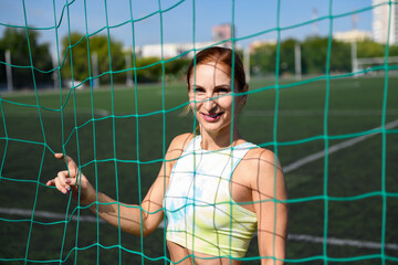Women and sport. Beautiful girl in summer sportswear stands behind the sports net and smiles on the green grass of a stadium. Middle aged sportswoman