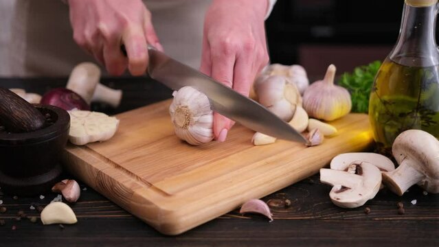 woman slicing garlic on wooden cutting board at domestic kitchen