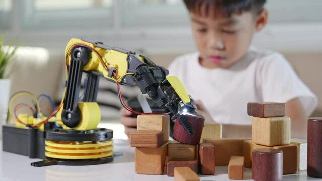 Happy Asian little kid boy using remote control playing robotic machine arm for pick up wood block, Funny child learning successful getting lesson control robot arm, Technology science education