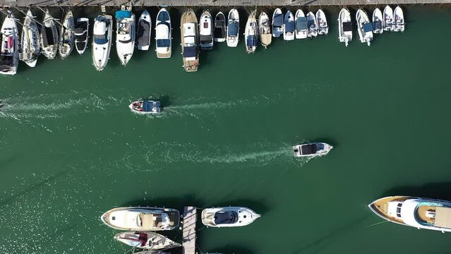 Boat traffic in a Latchi port passing moored yachts, aerial downwards view
