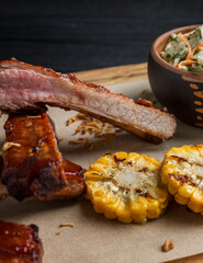 Fried lamb ribs with corn. An appetizing dish is served on a wooden board. Close-up.