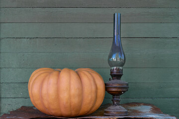 The pumpkin stands on a gray background, on a rusty iron sheet. Next to the pumpkin is an old, cobweb-covered kerosene lamp with a sooty shade. Selective focus.