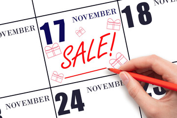 Hand writing text SALE and drawing gift boxes on calendar date November 17. Shopping Reminder