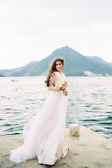 Bride with a bouquet stands on the pier against the backdrop of the mountains