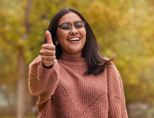 Thumbs up, support and woman with smile in a park for peace, relax and happiness. Portrait of a happy, young and winning girl with hand sign for thank you, motivation and agreement in nature