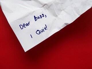 On red background, crumpled paper with handwritten text DEAR BOSS I QUIT, concept of employee...
