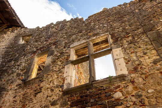 Old medieval stone facade. The wall is broken and looks like a ruin. Blue sky and warm light on the stones. Old windows that makes a romantic atmosphere. P&eacute;rouges, Ain, Auvergne Rh&ocirc;ne Alpes, France.