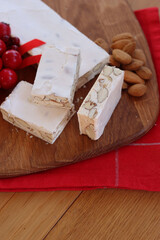 Traditional italian festive Torrone di Cremona ( white Nougat) with almonds cut in pieces on a wooden cutting board on table with Christmas decorations