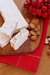 Traditional italian festive Torrone di Cremona ( white Nougat) with almonds cut in pieces on a wooden cutting board on table with Christmas decorations
