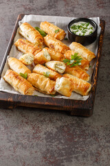 sigara boregi is a famous Turkish deep-fried pastry crispy rolls of thin dough are stuffed with a creamy mixture of cheese and parsley closeup on the wooden board on the table. Vertical