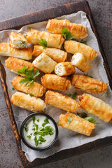 sigara boregi is a famous Turkish deep-fried pastry crispy rolls of thin dough are stuffed with a creamy mixture of cheese and parsley closeup on the wooden board on the table. Vertical top view 