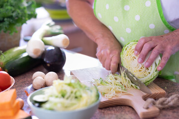 Close-up on senior woman's hand slicing a cabbage while preparing vegetables in home kitchen. Healthy, vegan or vegetarian lifestyle