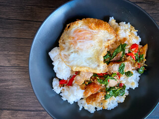 Rice topped with stir-fried pork and basil with a fried egg on the table