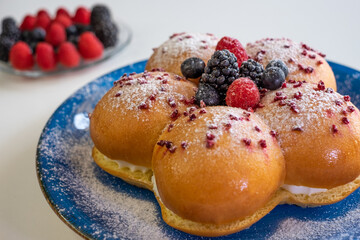 Home cooking concept. Fresh organic homemade sweet soft milk bread filled with cream and decorated with berries, on blue dish