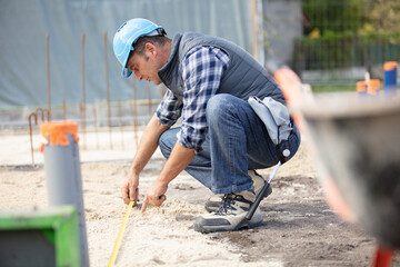 construction worker measuring foundations at site - Powered by Adobe