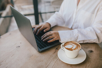 Young woman drinking coffee working online using her laptop.