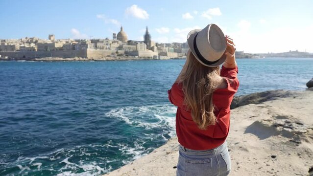 Portrait of young woman on waterfront looking at camera with Valletta city on the background, Malta Island