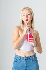 Young attractive blonde woman in a white top and blue jeans with a cocktail in her hands on a white background